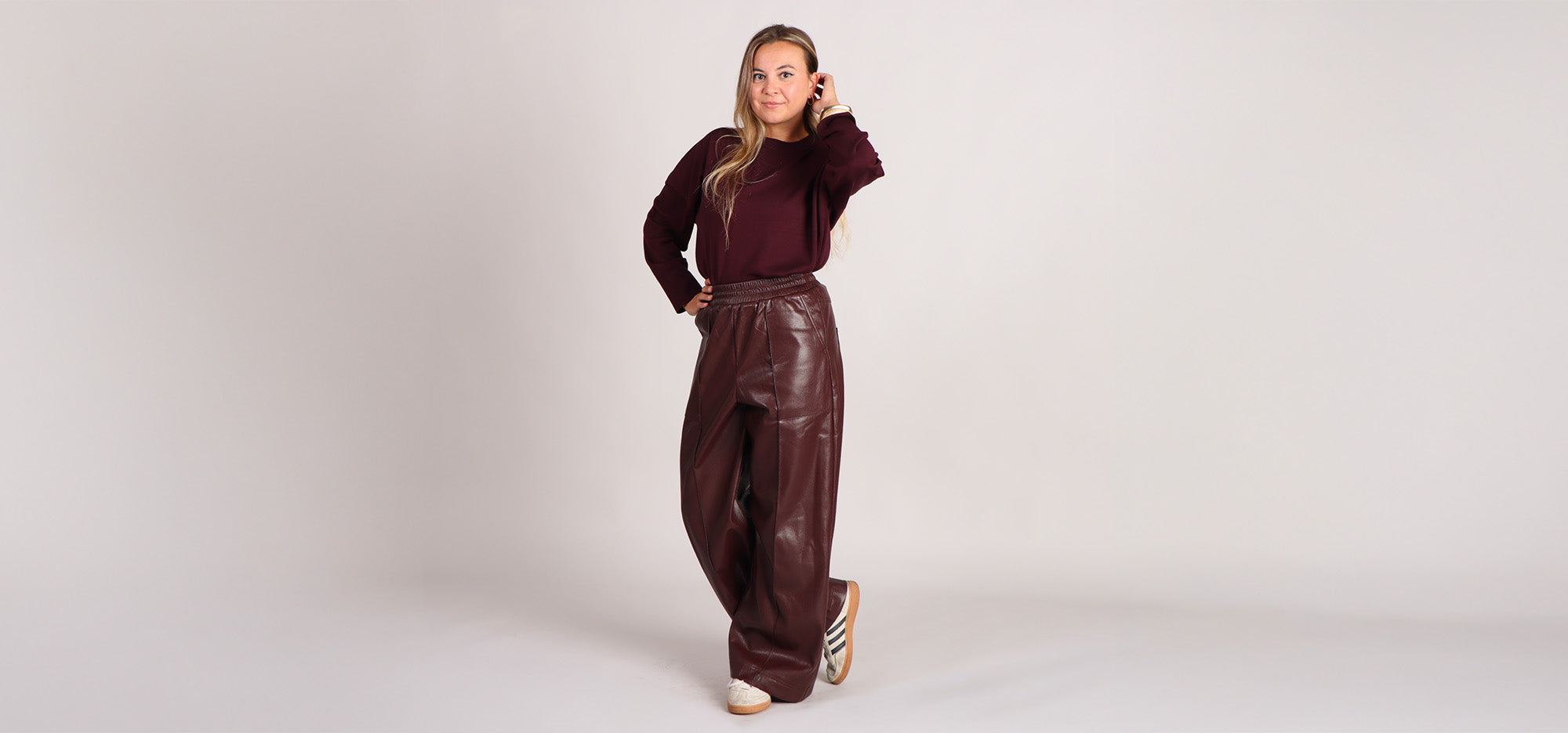 Model draagt bordeauxrode knit en vegan leather bordeaux rode broek. De perfecte herfst/winter look van 2025/2026.