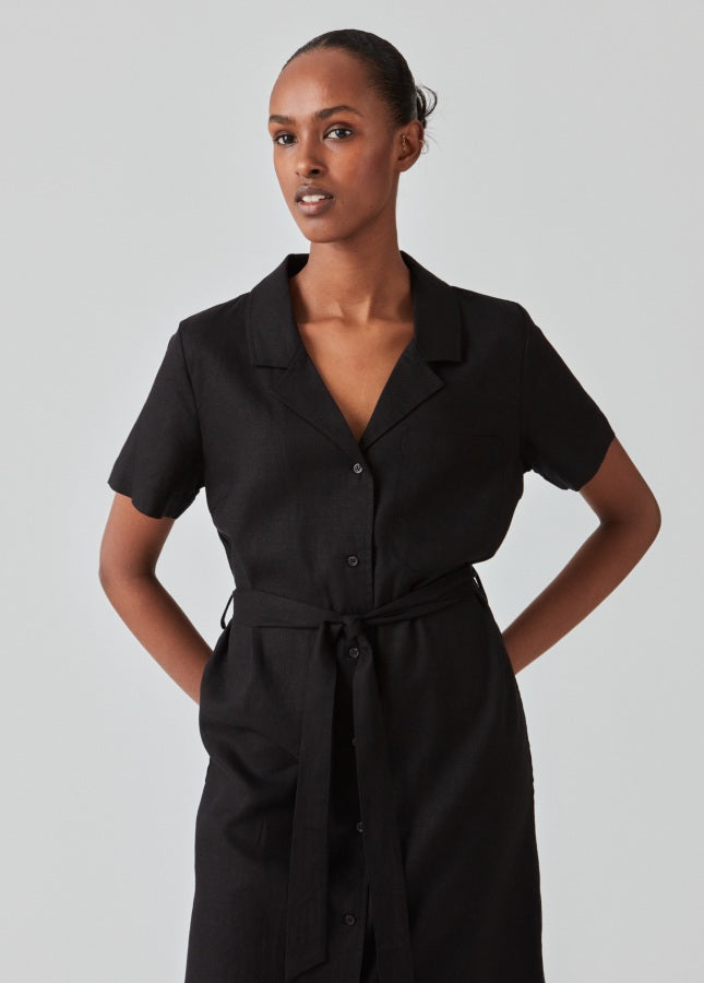 Zwarte linnenmix blousejurk van het merk Modstrom. De zwarte midi-jurk Darrel heeft een resortkraag, korte mouwen, een borstzakje, knopen aan de voorkant. De zwarte jurk heeft een brede strikceintuur in de taille, waardoor je de jurk mooi kunt tailleren. De perfecte zomerjurk. Shop de nieuwe collectie jurken online.